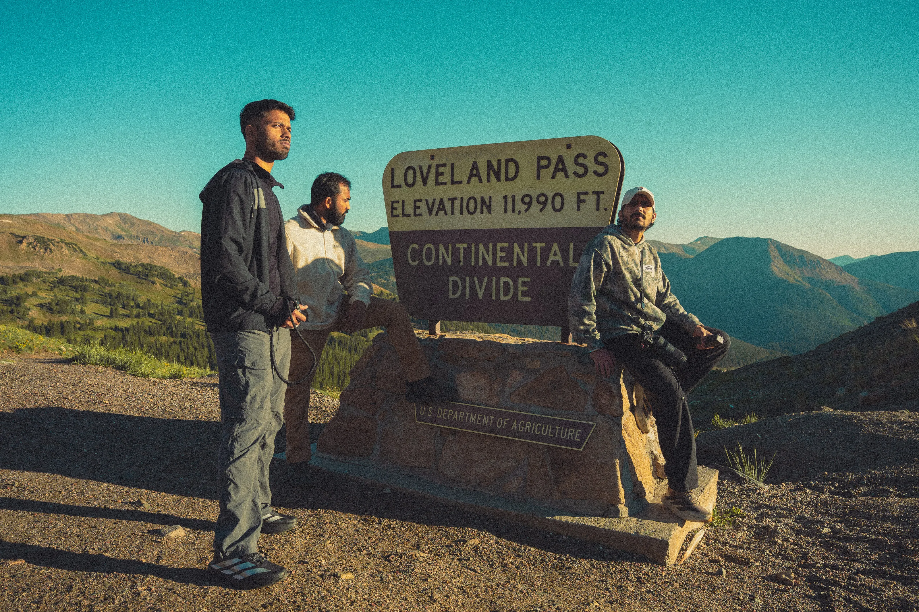 Three friends lean on the Loveland Pass sign, elevation 11,990 feet, on the Continental Divide.