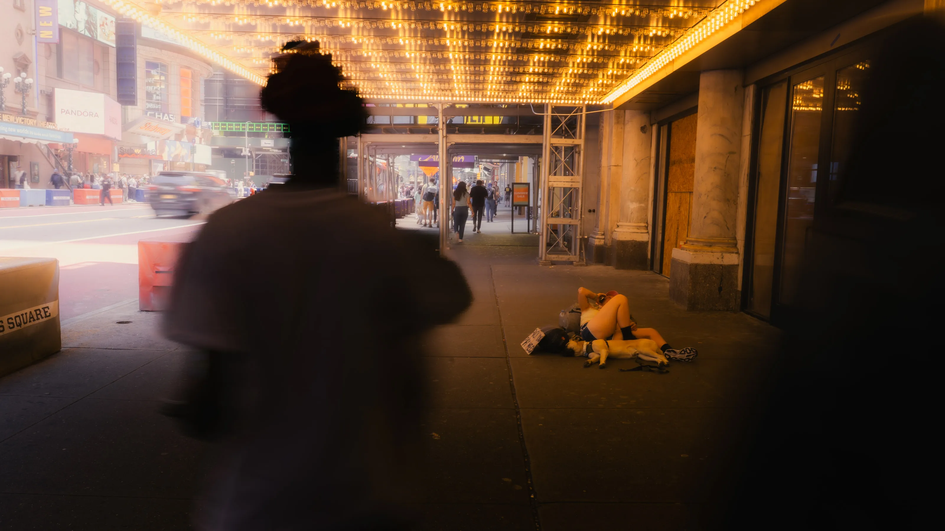 A figure in silhouette walks under a theatre marquee of warm bulbs.