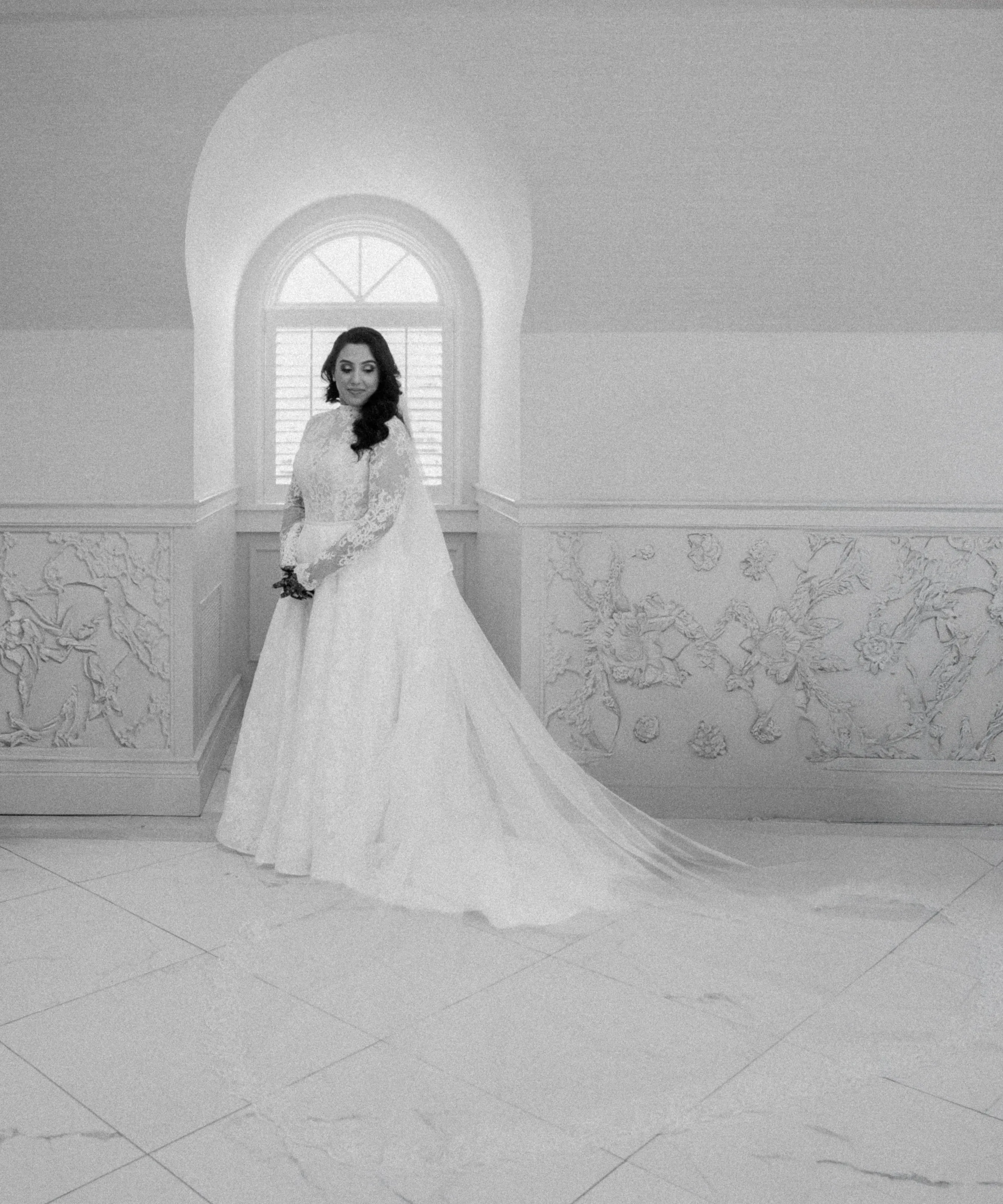 Black-and-white portrait of the bride in a white gown beneath an arched window.