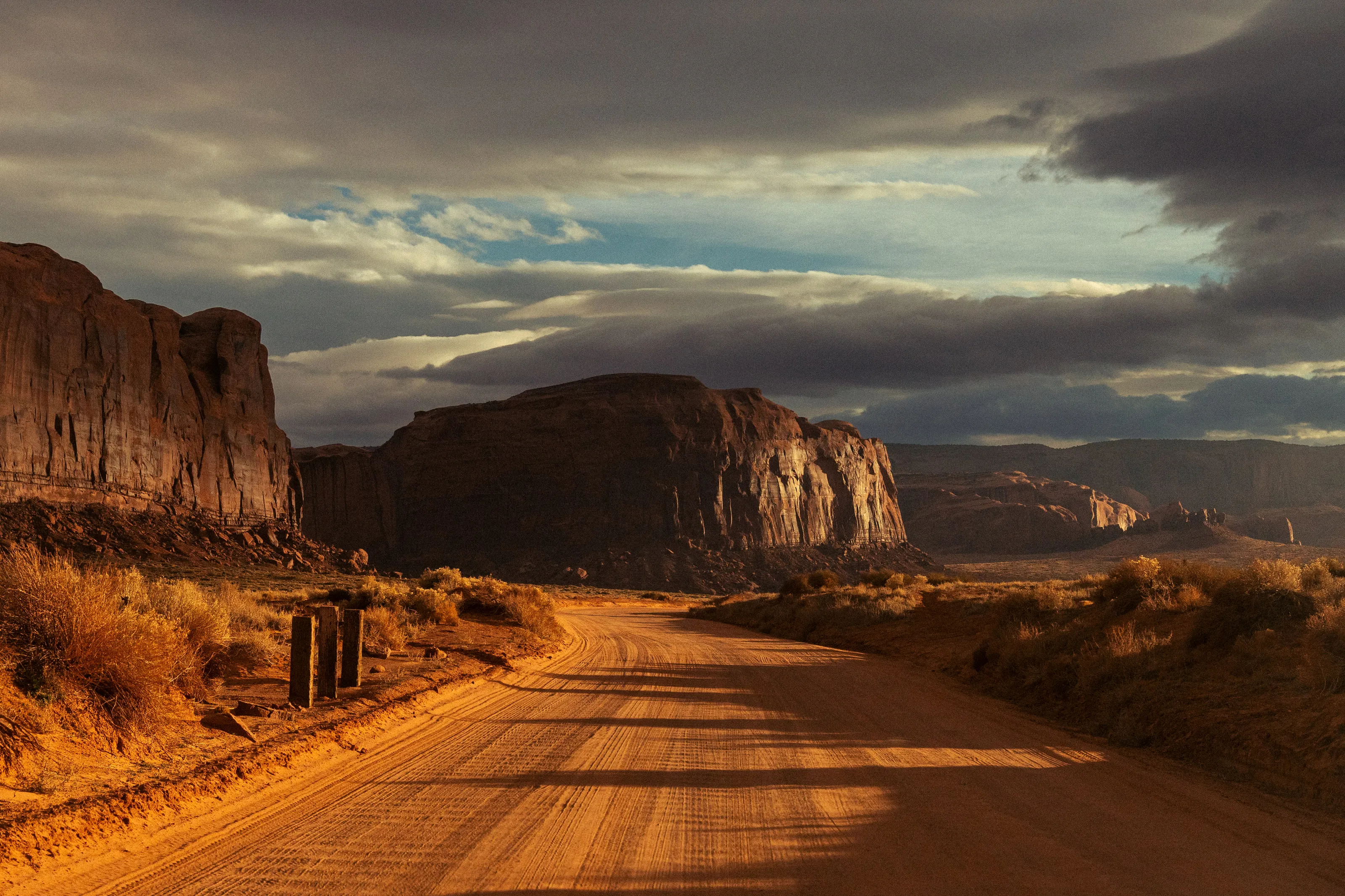 A dirt road runs toward red cliffs in low, raking light.