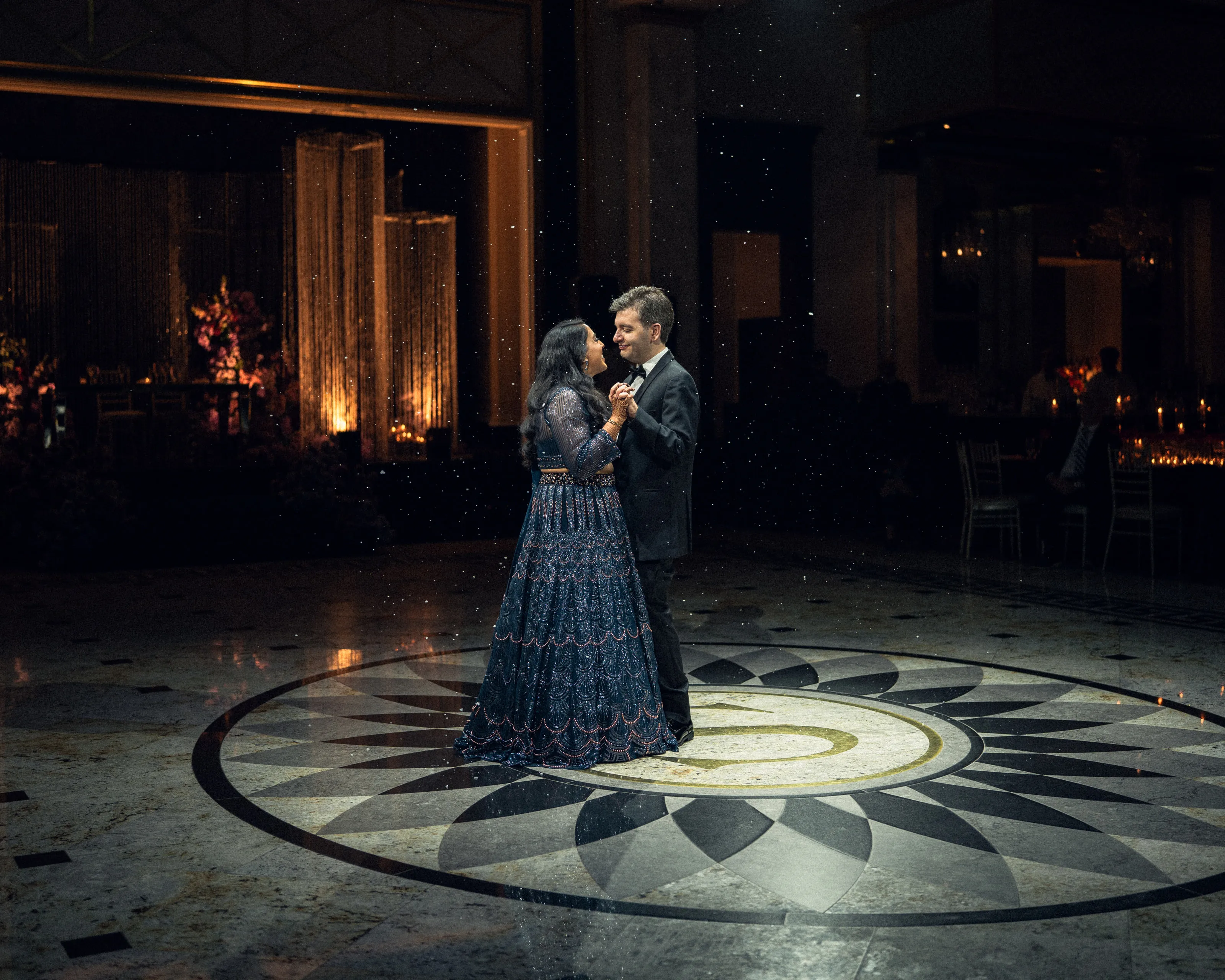 The couple share a first dance on a patterned marble floor in a dark ballroom.