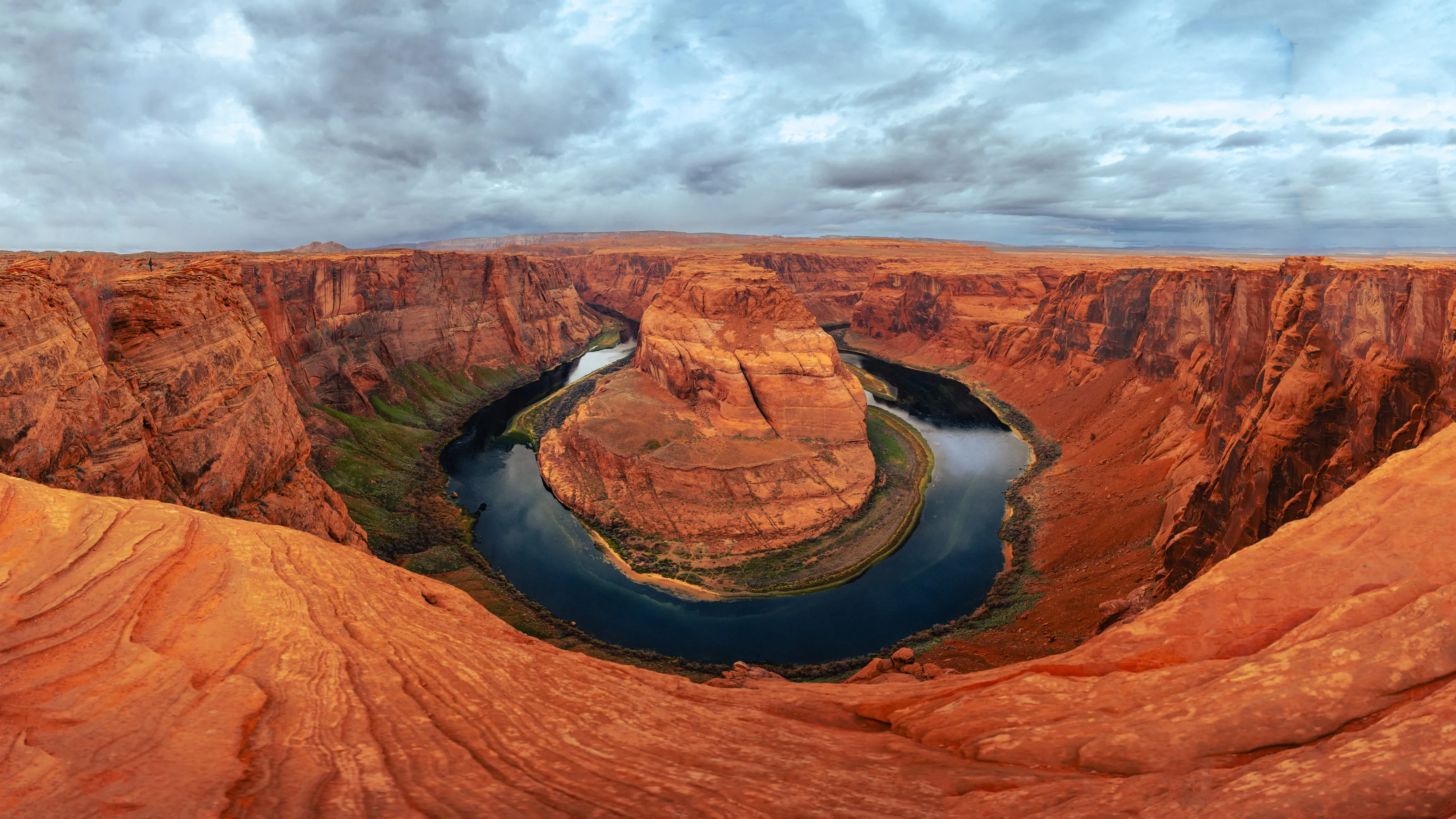 The Colorado River curves around Horseshoe Bend, seen from the rim in a wide panorama.