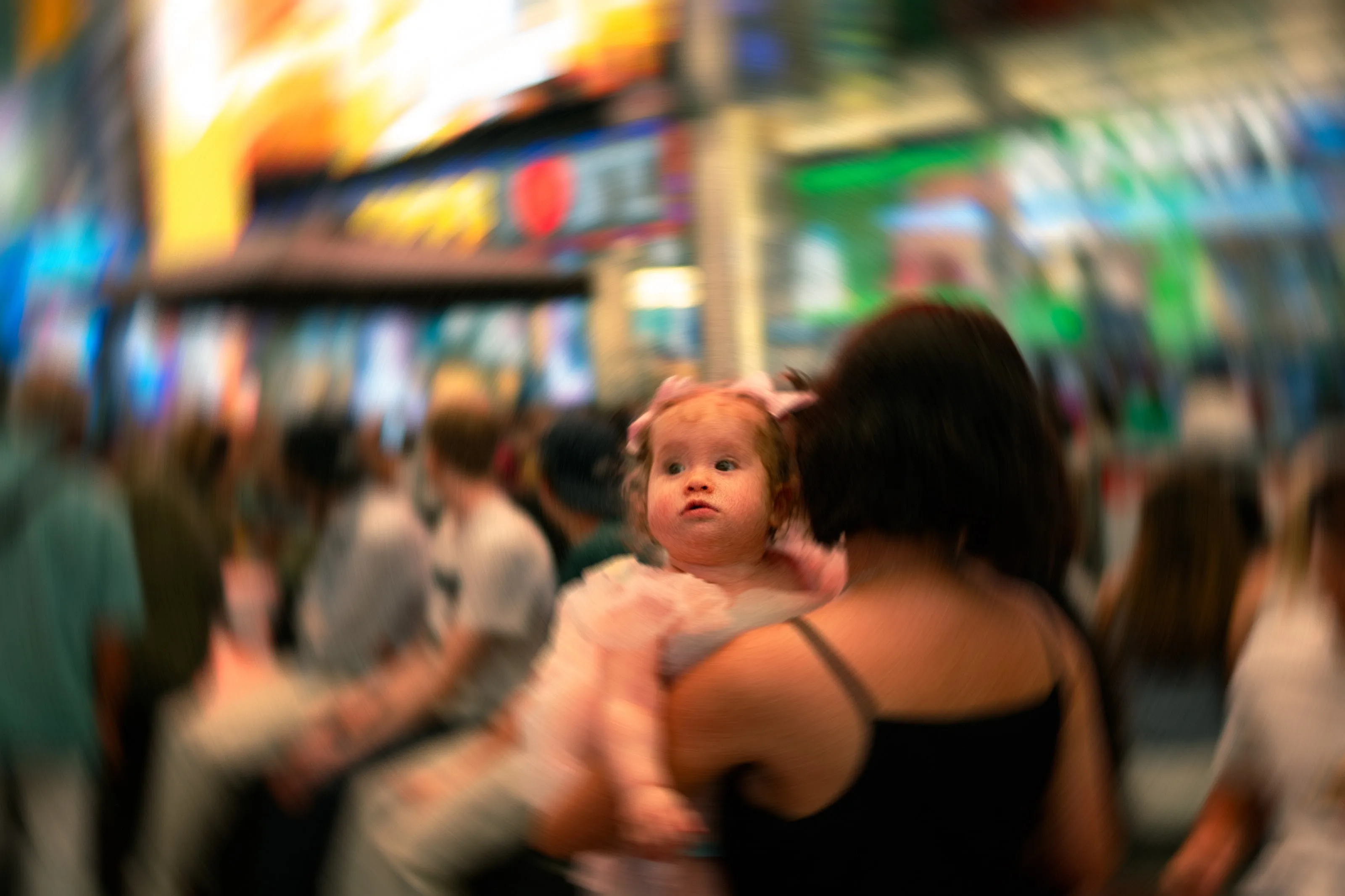 A baby looks over a shoulder in a blurred, neon-lit crowd.