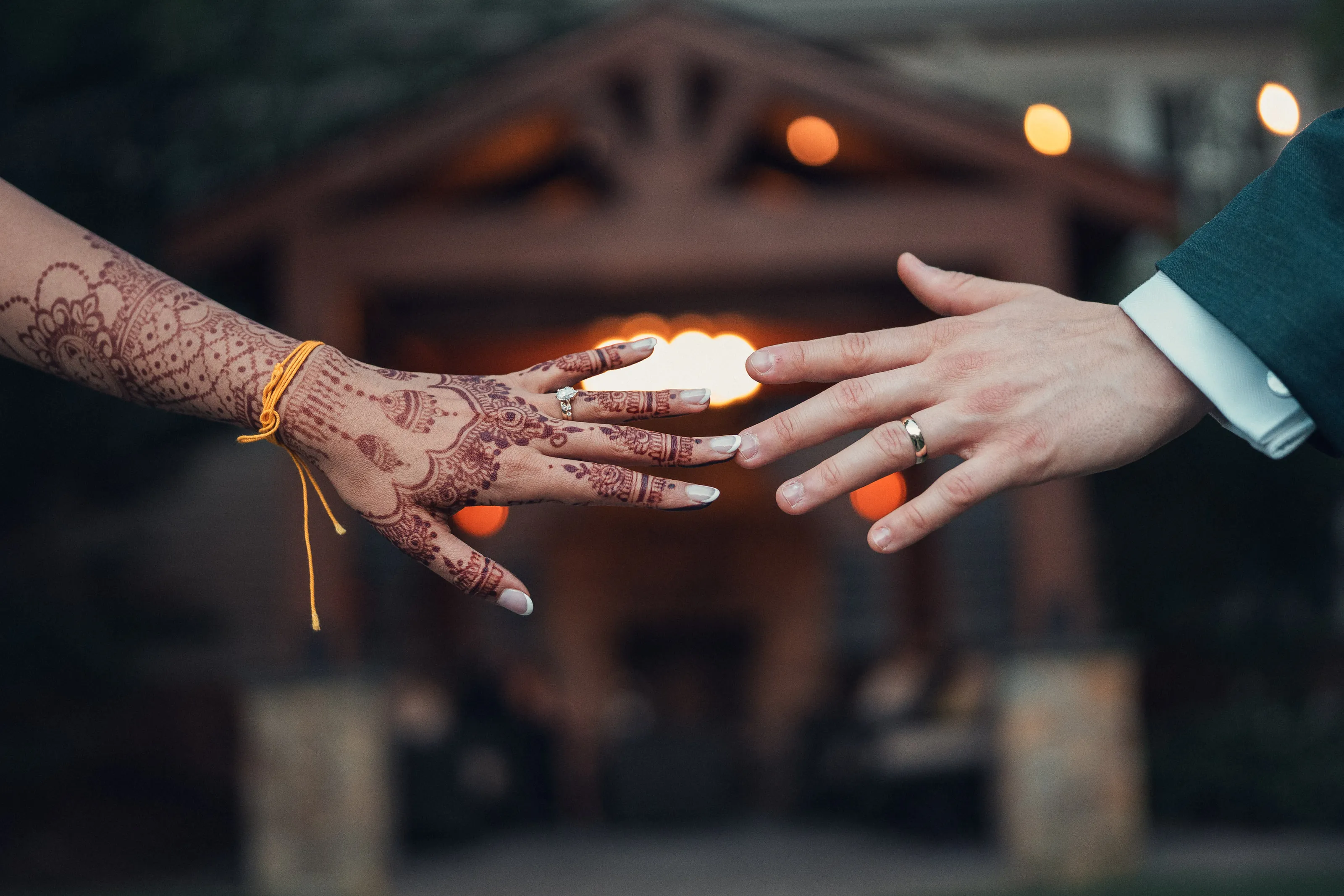 Close-up of two hands, one with henna, touching fingertips in front of string lights.